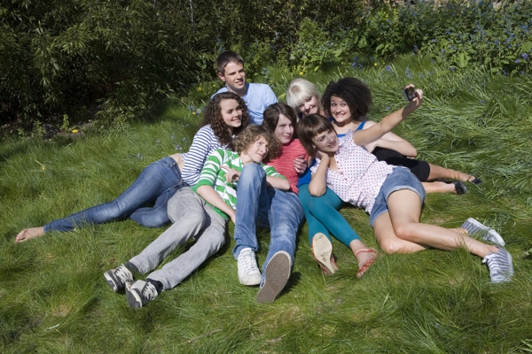坐在草地上一起照相的年轻人图片