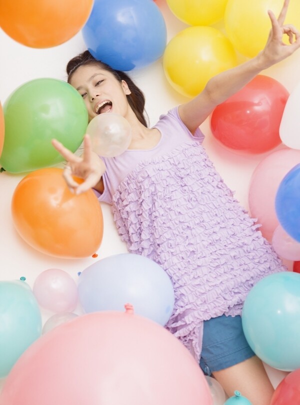 躺在彩色气球中伸出胜利手势的美女图片